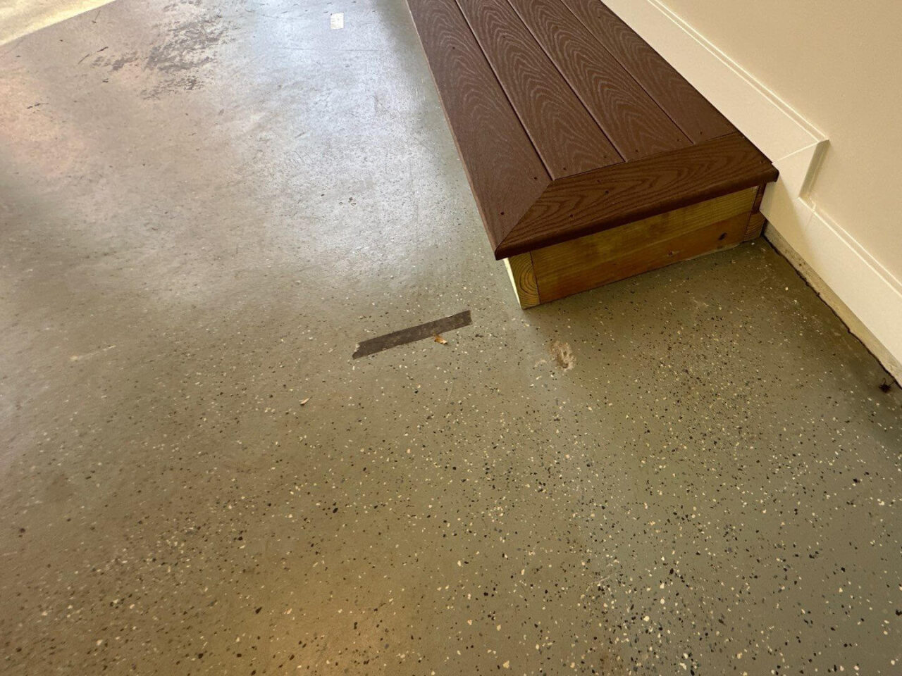 Close-up of wooden step next to the garage floor showing prior flake-painted coating.