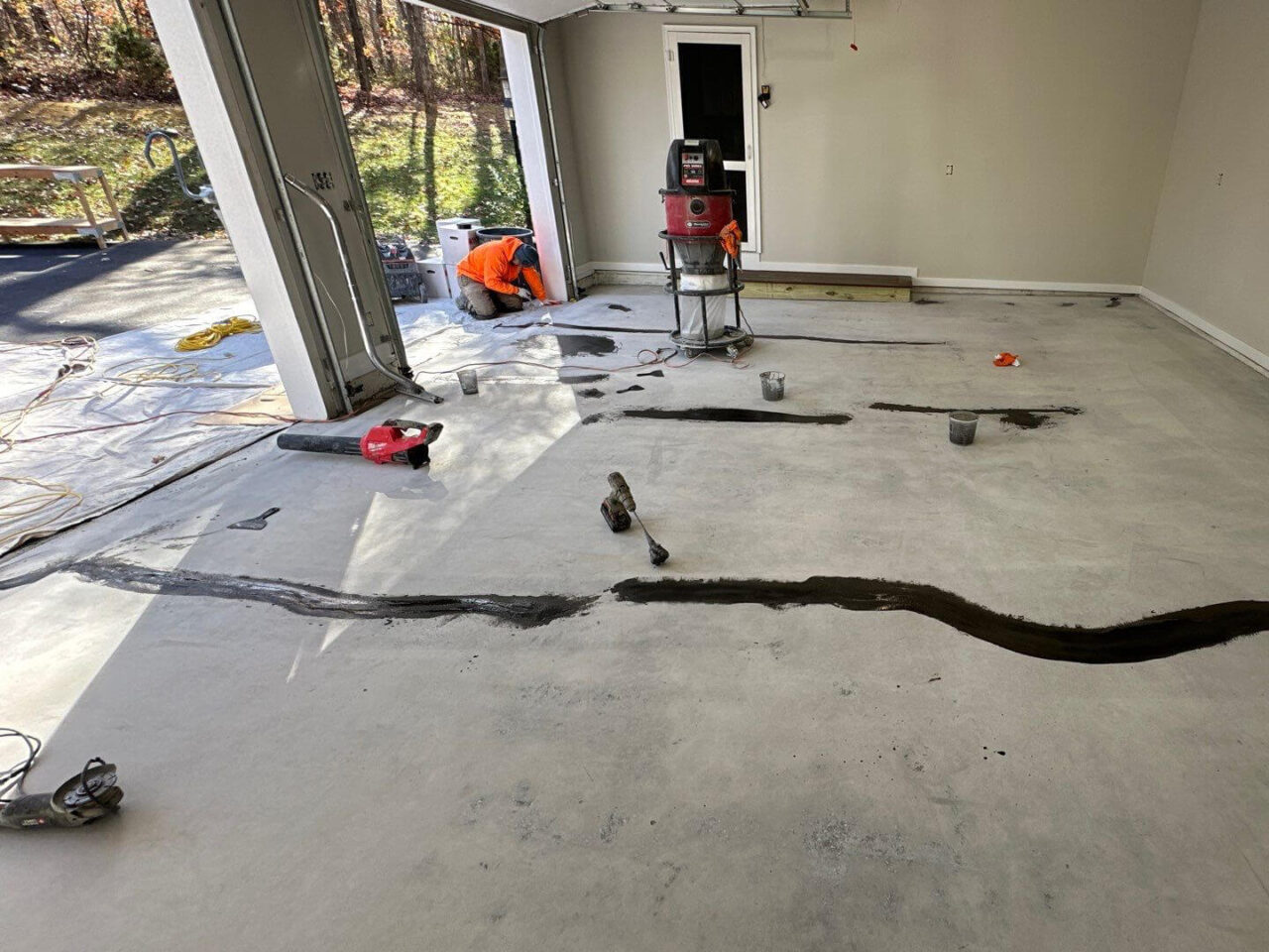 Garage floor before coating showing extensive crack repair and surface prep underway.