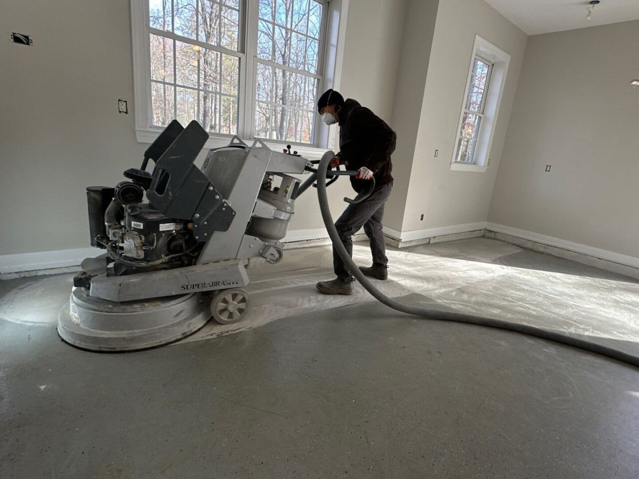 Installer operating large floor grinder on garage slab during early surface prep stage.