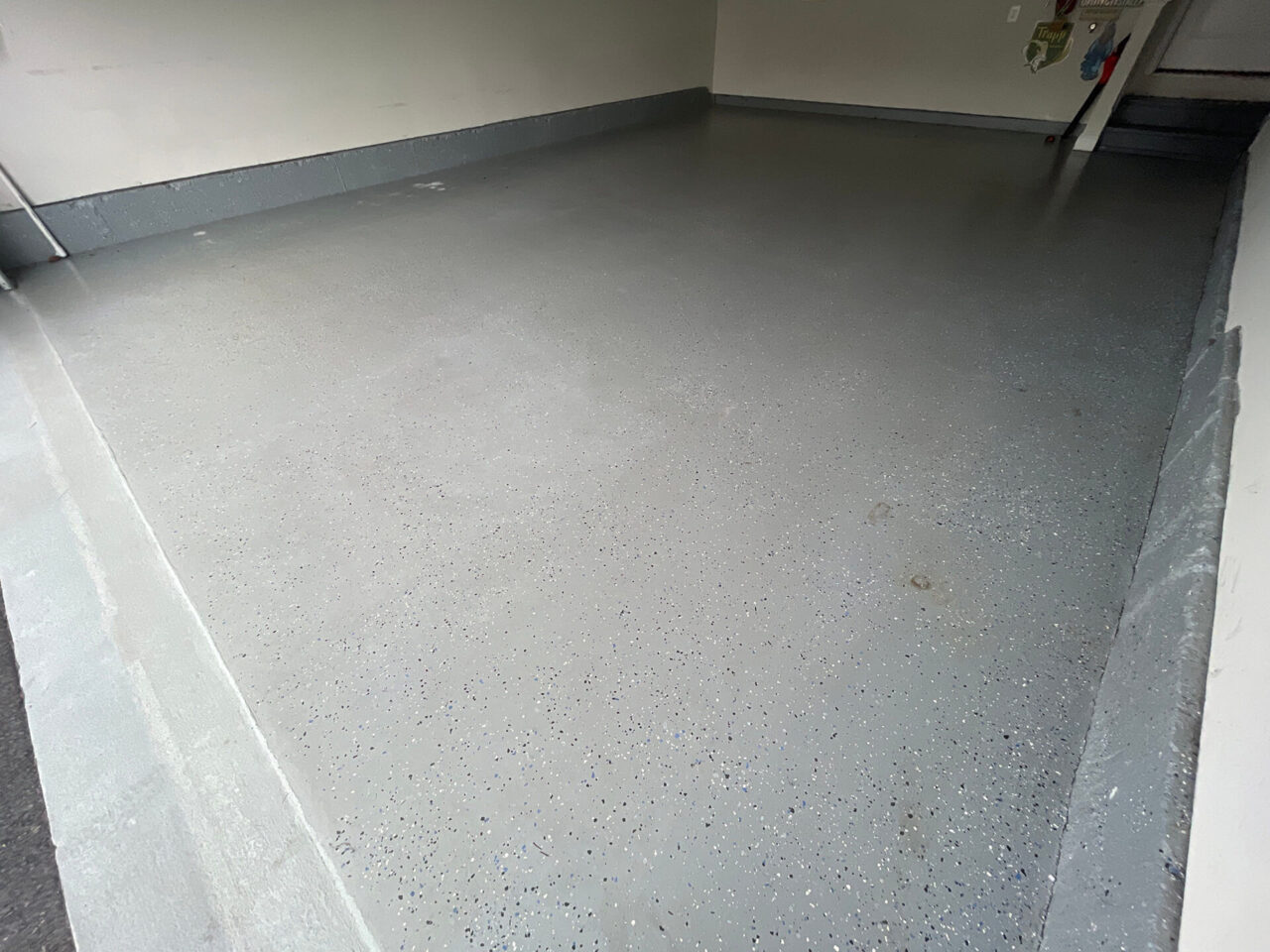 Before shot of garage corner with uneven DIY epoxy and dark tire marks near the wall.