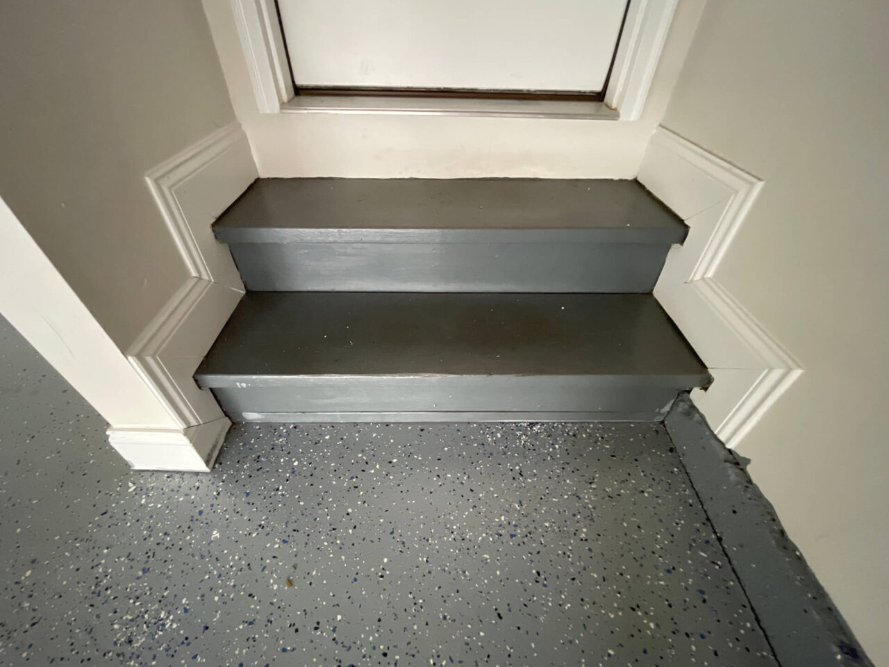 View of garage stairs and lower wall before refinishing, showing chipped paint and aging coating.